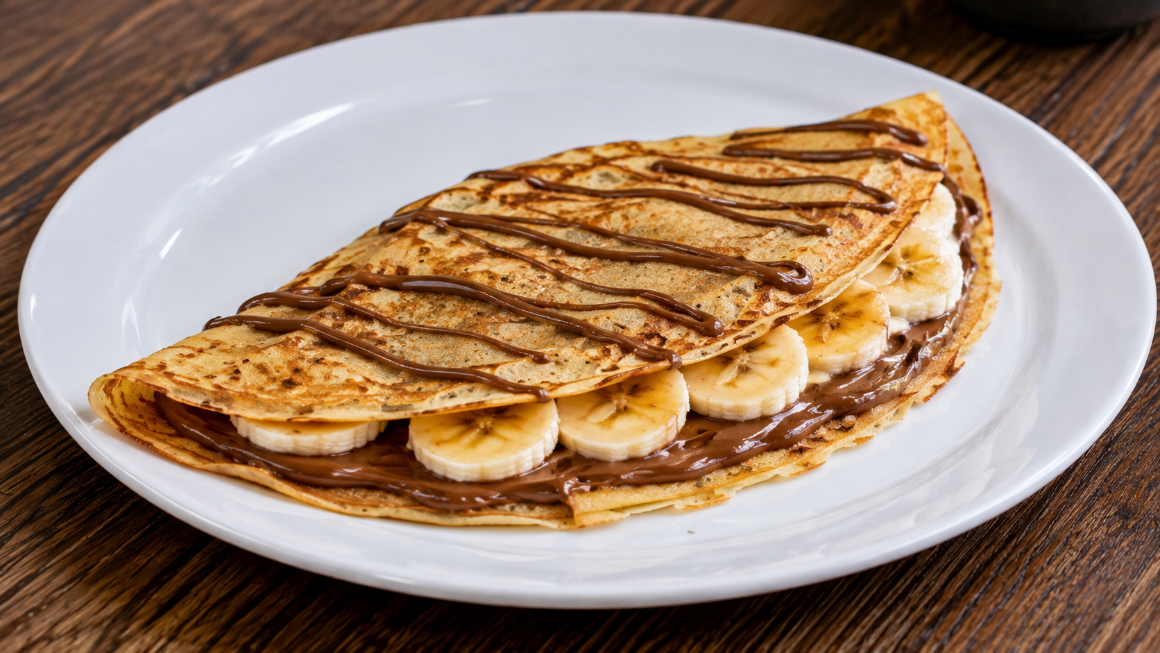 Fotografia de um crepe doce recheado com banana e creme de avelã, servido em prato branco.